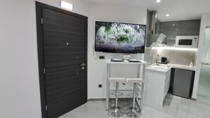 A modern kitchen with a built-in microwave, a glass-top bar stool, and a flat-screen TV mounted on the wall. - KM LUXURY apart downtown (Heraklion)