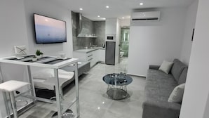 A modern, compact living space with a kitchenette, a sofa, a dining table, and a TV mounted on the wall. - KM LUXURY apart downtown (Heraklion)