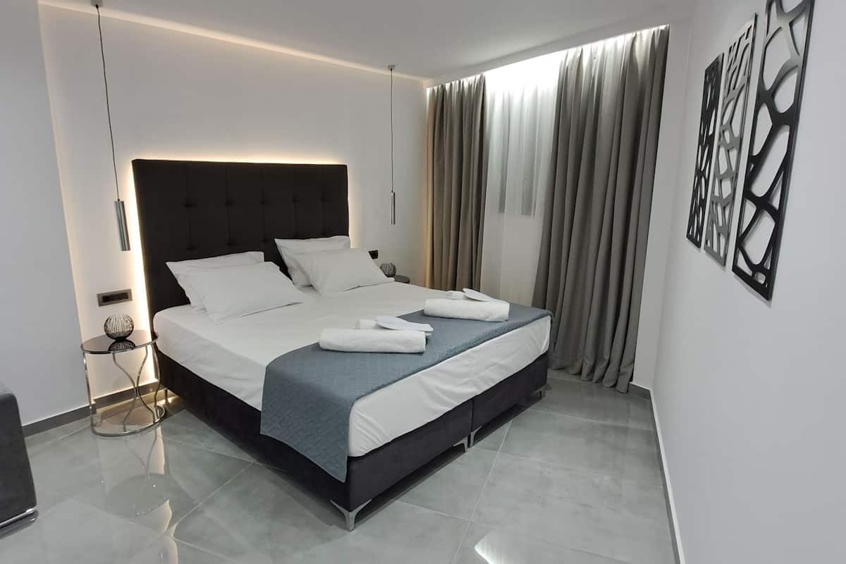 A modern bedroom with a large bed, a grey sofa, and a bedside table.