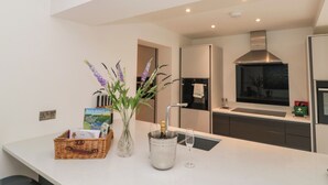 A modern kitchen with a white countertop, a vase with flowers, a wine glass, and a basket of books. - Bailey House (Driffield)