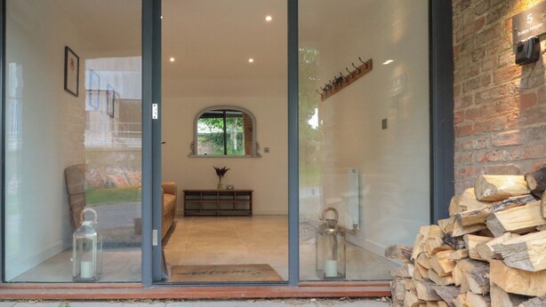 A modern interior with a glass door leading to a living area, a fireplace, and a stack of firewood. - Bailey House (Driffield)
