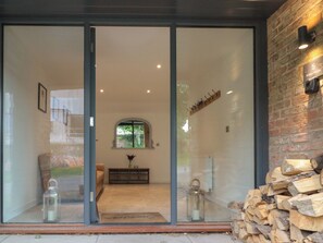 A modern interior with a glass door leading to a living area, a fireplace, and a stack of firewood. - Bailey House (Driffield)