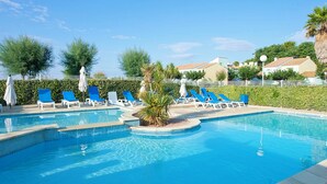 Una piscina con sillas de descanso azules y sombrillas, rodeada de vegetación y edificios.