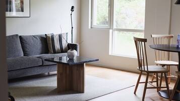 A modern living room with a grey sofa, a wooden coffee table, and a dining area with wooden chairs and a small table.
