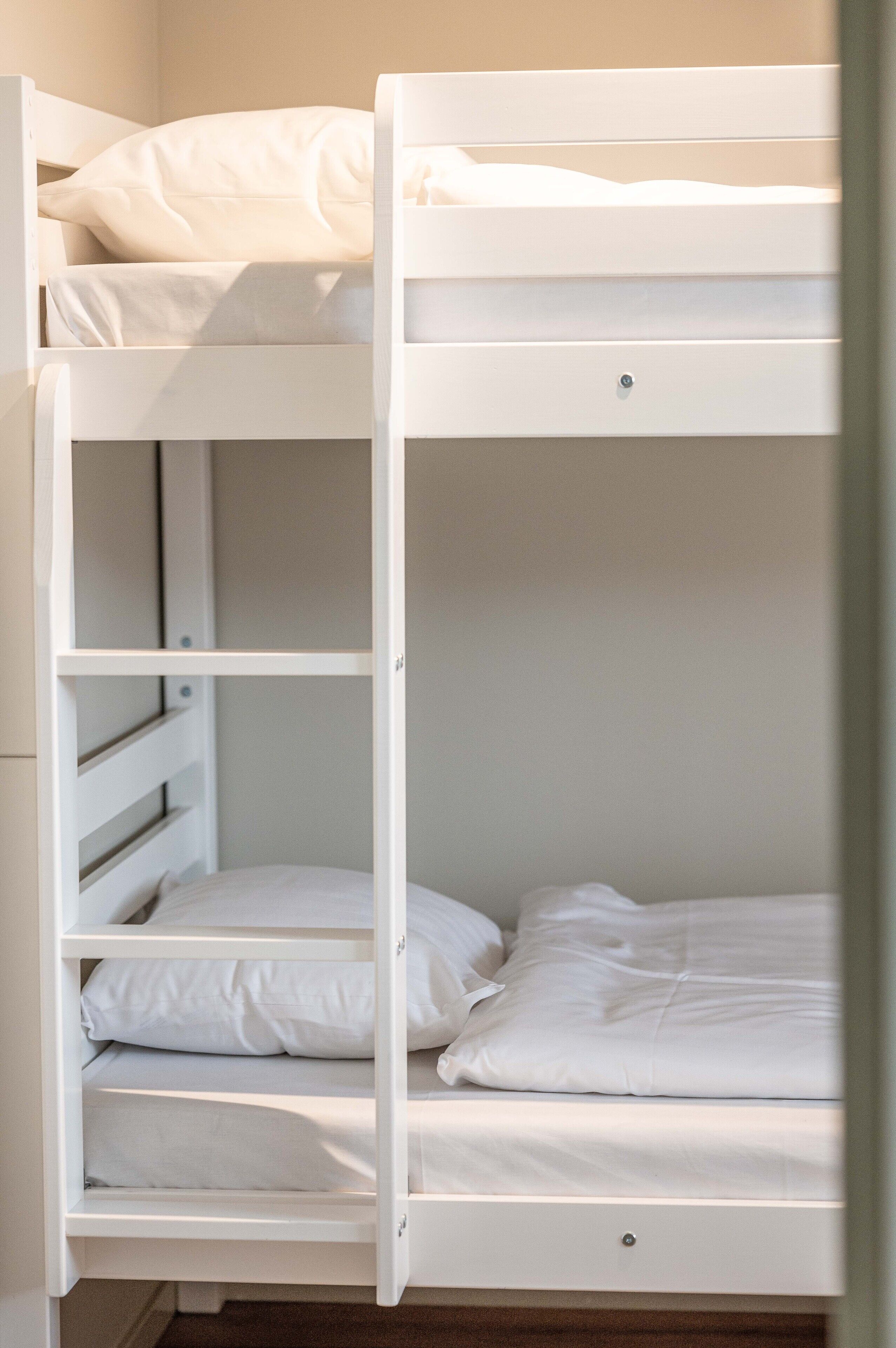A bunk bed with white bedding and a drawer below.