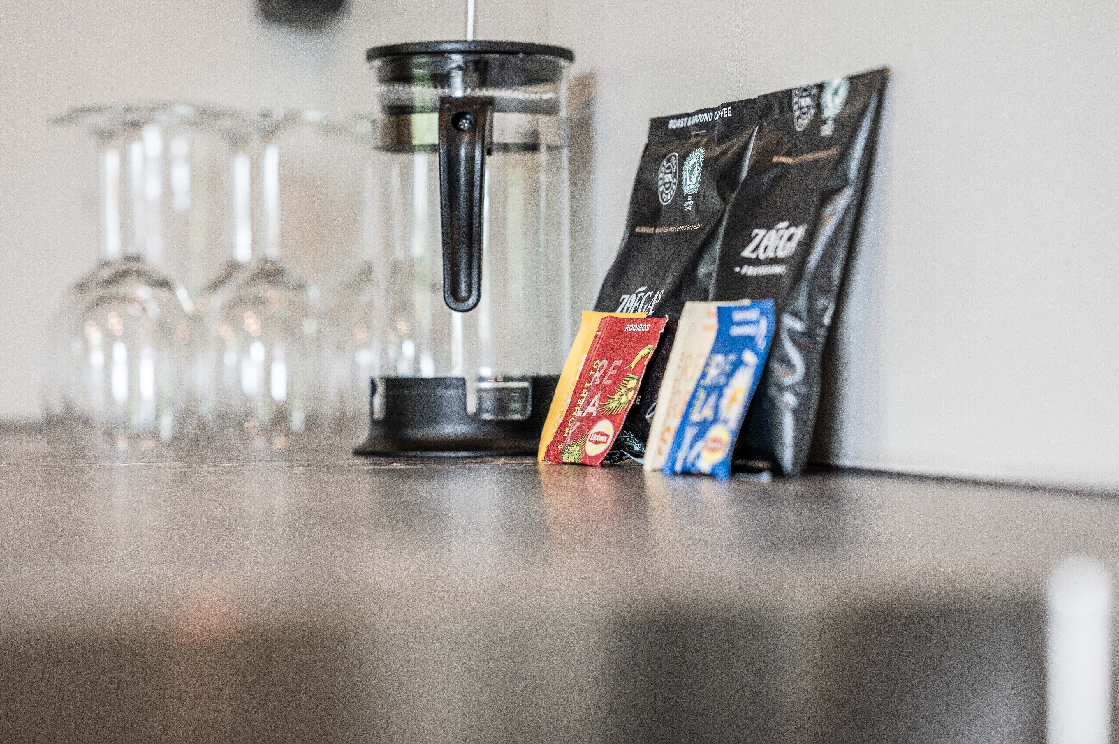Eine Kaffeemaschine, eine Glas-Kanne und Kaffeepäckchen auf einer Arbeitsplatte.