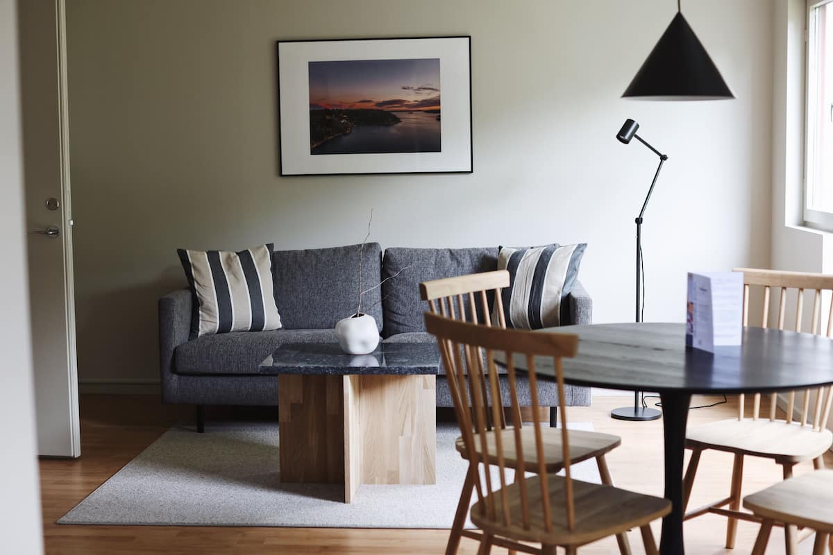A modern living room with a gray sofa, wooden chairs, a round table, and a framed picture on the wall.
