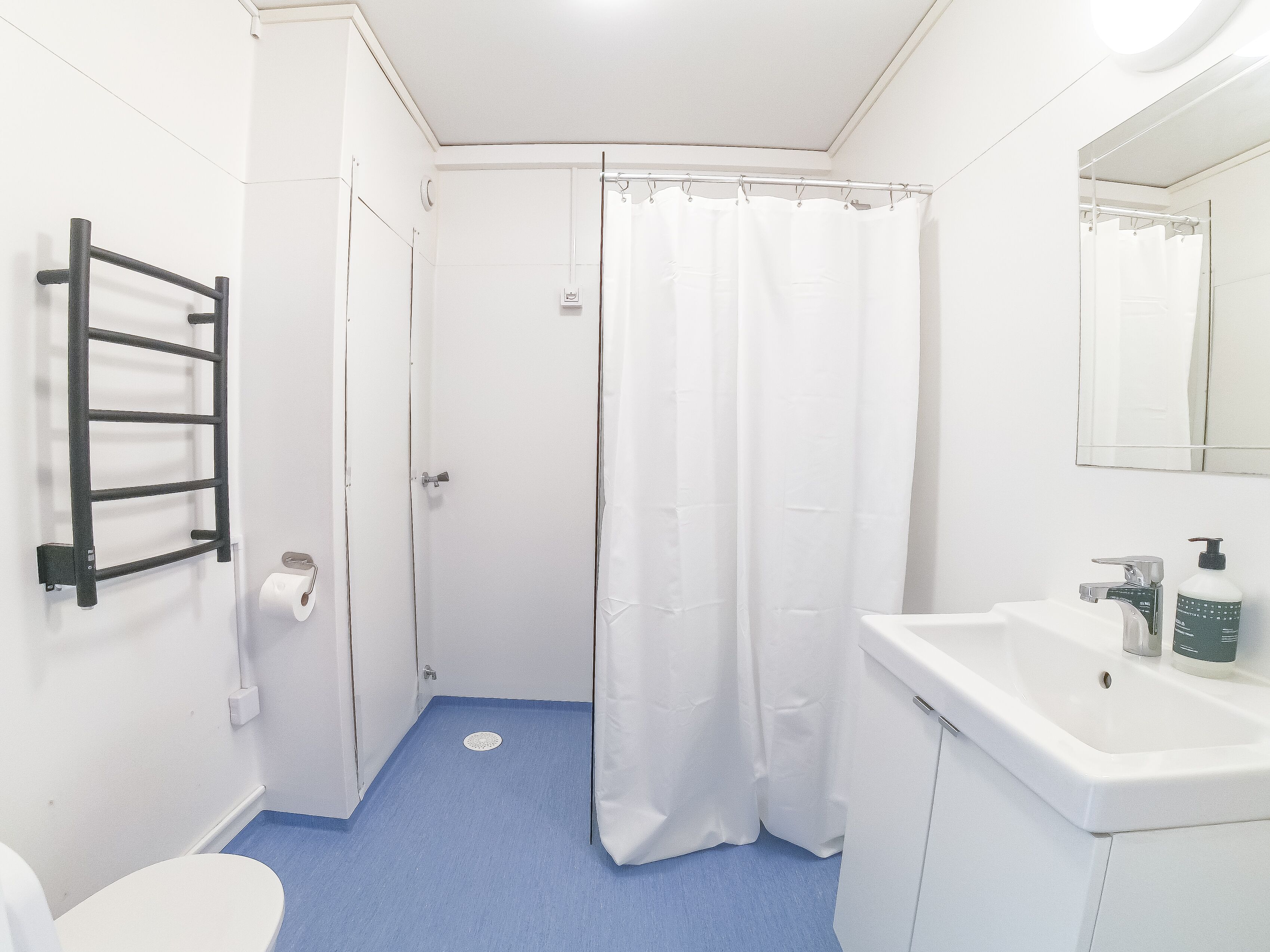 Un baño con lavamanos blanco, espejo, cortina de ducha y toallero.