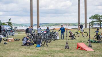 A group of people around bicycles and a truck, with a grassy field and a body of water in the background.