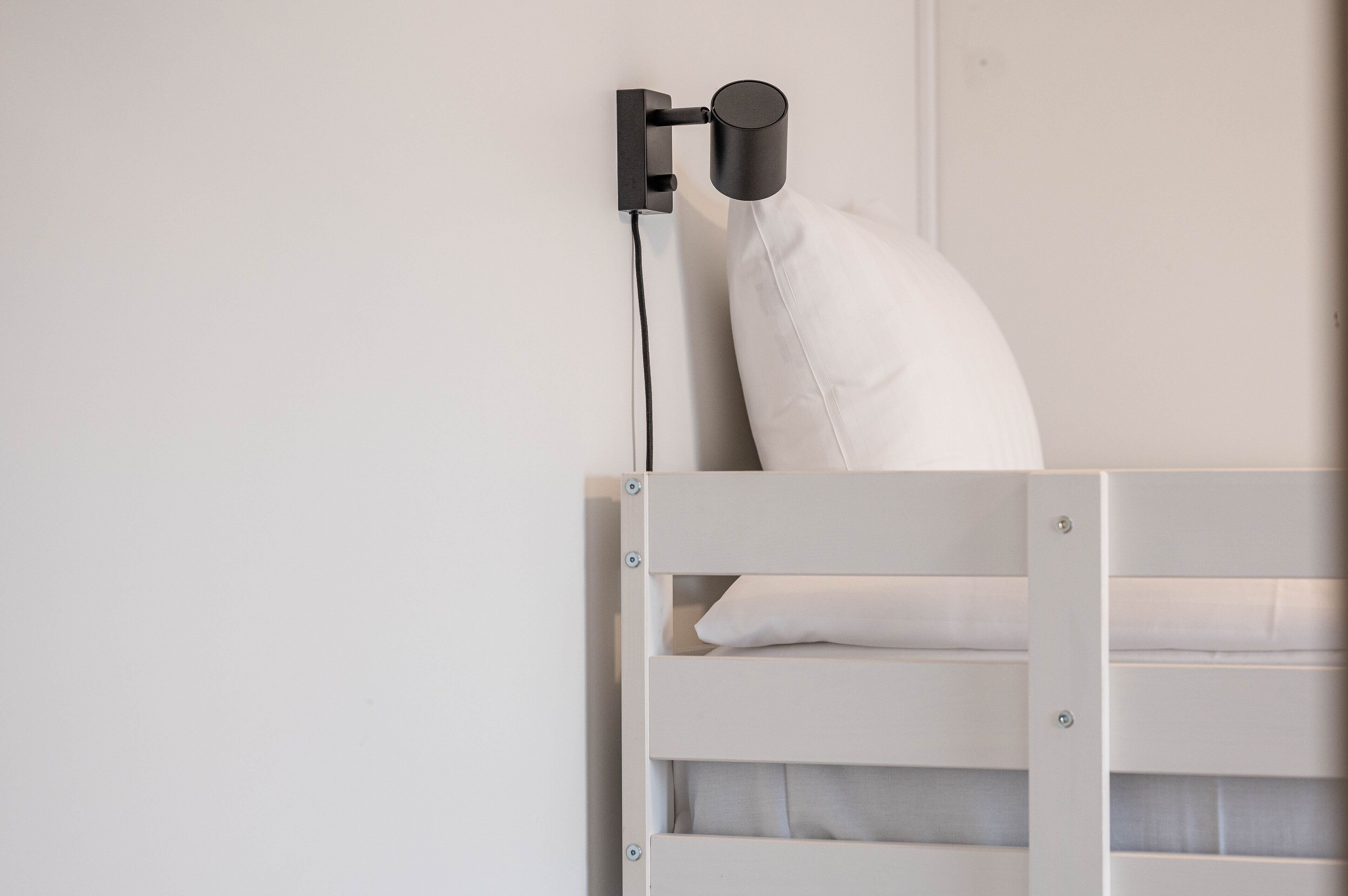 Ein weißes Bett mit Kissen und einem schwarzen Gegenstand an der Wand darüber.