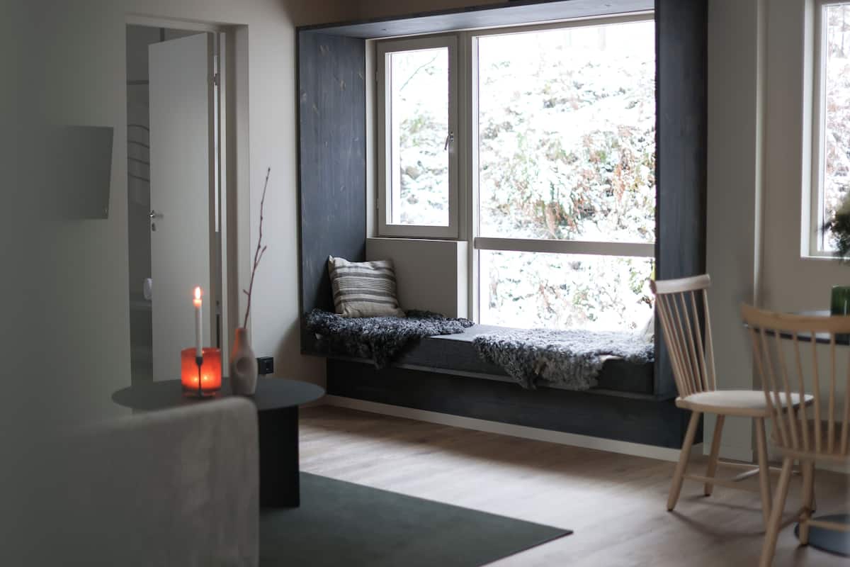 A room with a built-in bench by a window, a small table with candles, and a chair.