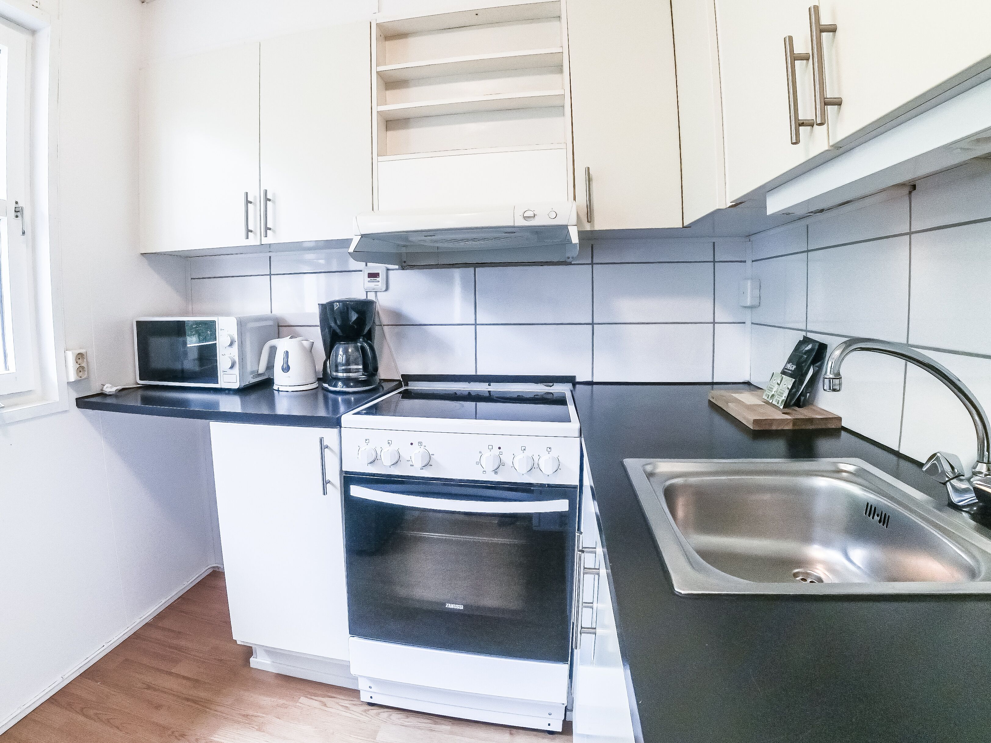 A compact kitchen with white cabinets, a microwave, a coffee maker, a stove, and a sink.