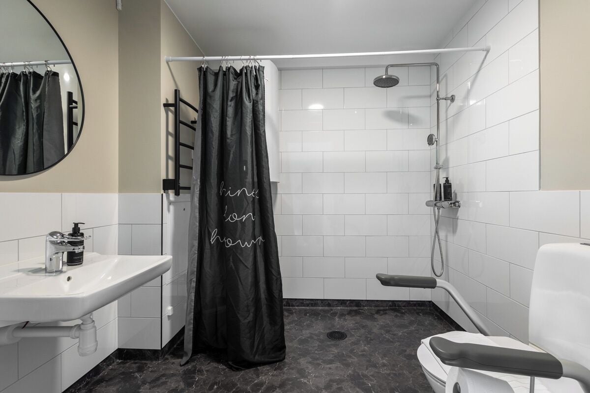 A modern bathroom with a white sink, a shower with a handheld showerhead, and a black shower curtain with text.