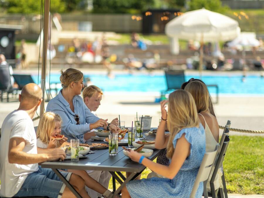 A group of people dining at an outdoor table with a pool in the background.