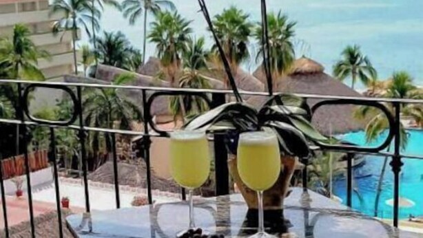 A balcony with a table set for two, overlooking a pool and palm trees.