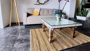A modern living room with a glass coffee table, a beige sofa, a floor lamp, and potted plants.