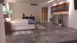 A modern bedroom with a large bed, bedside tables, a nightstand, a painting on the wall, and a potted plant.