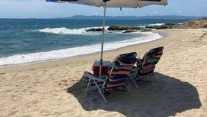 A beach with a blue umbrella and two colorful beach chairs.