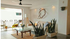 A modern living room with a glass coffee table, two potted plants, a sofa, and a decorative wall piece.