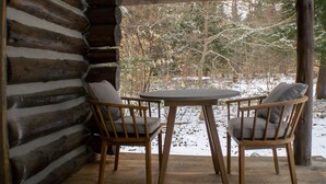 A log cabin with two wooden chairs and a table, a wooden ceiling, and a view of a snowy forest. - Seclude in a Romantic Cabin in an 850 acre Private Forest. (Bernhards Bay)
