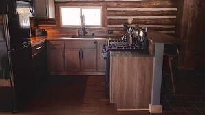 A rustic kitchen with wooden beams, a built-in stove, and a sink. - Seclude in a Romantic Cabin in an 850 acre Private Forest. (Bernhards Bay)