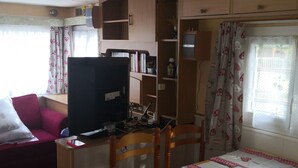 Un espacio habitable compacto con una mesa de comedor, sillas, un televisor y una estantería.