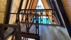 A wooden attic room with a sloped ceiling, wooden beams, and a view of a swimming pool. - Olive Garden  (Konyaalti)