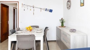 Un comedor con una mesa blanca preparada para cuatro personas, un frutero y una guirnalda decorativa de luces.