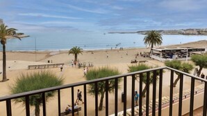Vista de la playa desde un balcón, con palmeras, arena y un edificio con terraza.
