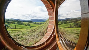 A view through a circular window with brick arches, overlooking a green landscape with fields and distant hills. - Badgers View (Rhayader)