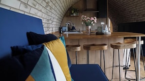 A cozy kitchen with a brick wall, wooden bar stools, and a blue sofa with colorful cushions. - Badgers View (Rhayader)