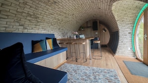 A cozy interior with a curved brick ceiling, a blue sofa, a wooden bar area, and a large window. - Badgers View (Rhayader)