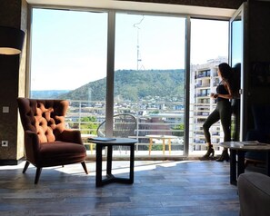 Un salon moderne doté d’une grande porte-fenêtre coulissante donnant sur un balcon avec vue sur la ville.