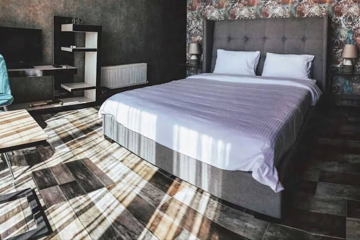 A modern bedroom with a large bed, a built-in TV, a seating area, and a patterned floor.