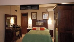 Une chambre à coucher comprenant un lit, une commode, un miroir et deux lampes fixées au mur.