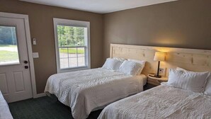 Une chambre d’hôtel avec deux lits, une porte, une fenêtre et une table de chevet avec une lampe.