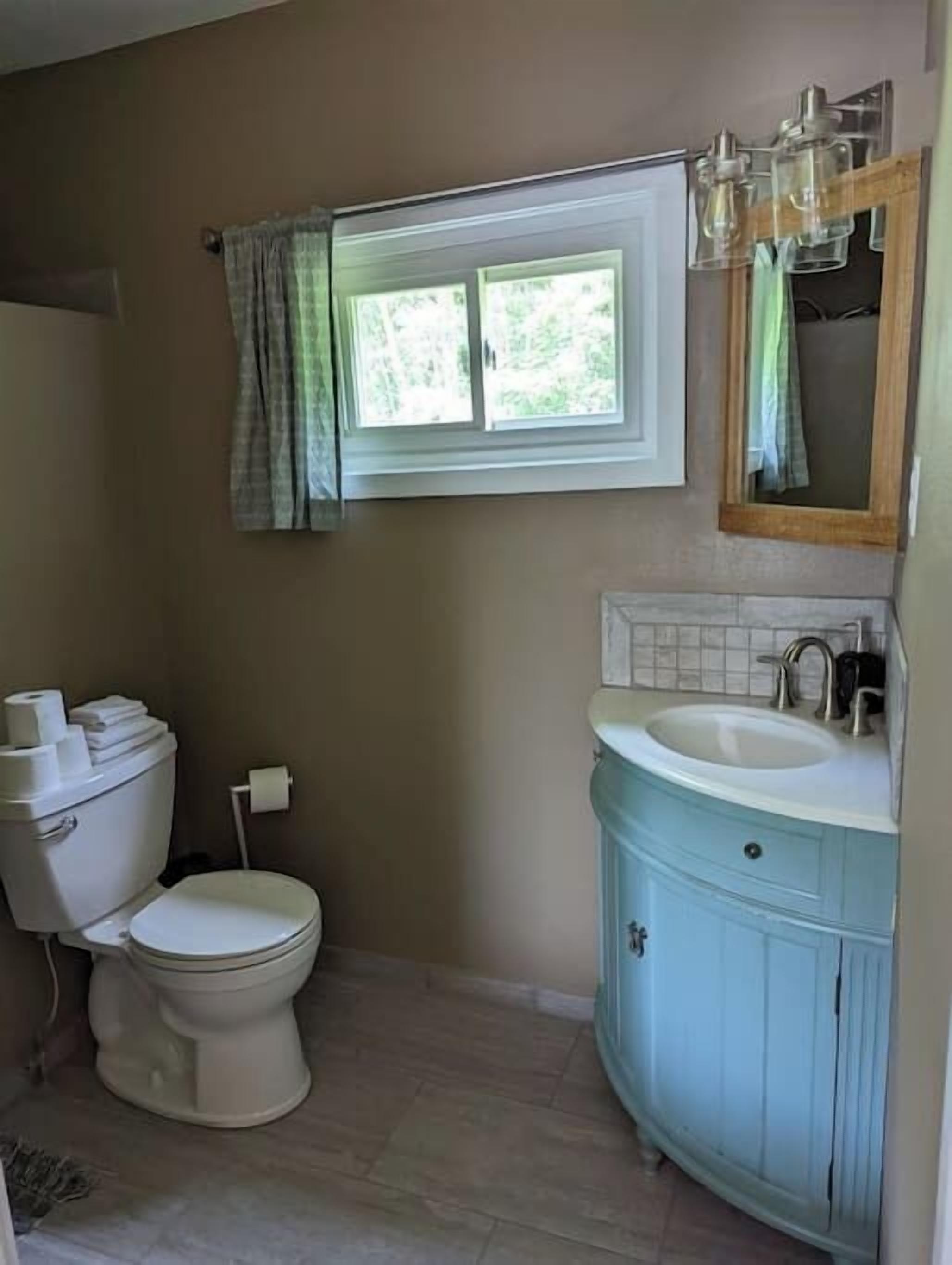 A bathroom with a toilet, sink, and window.