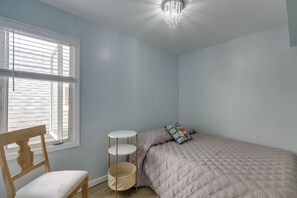 A bedroom with a bed, a chair, a bedside table, and a window with blinds. - Sunny Seaside Heights Retreat: Walkable Location! (Seaside Heights)