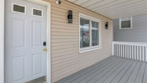 A covered porch with a white door, a window with blinds, and a small window with a view of a flag. - Seaside Heights Apartment Near Beach + Boardwalk! (Seaside Heights)