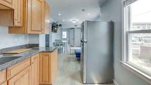A modern kitchen with wooden cabinets, a stainless steel refrigerator, and a window overlooking a street. - Seaside Heights Apartment Near Beach + Boardwalk! (Seaside Heights)