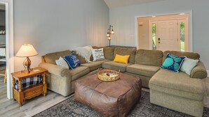 A living room with a sectional sofa, a brown leather ottoman, a side table with a lamp, and a floor lamp. - South Carolina Retreat w/ Fireplace & Lake Access! (Seneca)