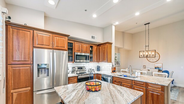A modern kitchen with wooden cabinets, stainless steel appliances, a marble countertop, and a hanging light fixture. - Elegant Naples Condo w/ Golf View & Community Pool (Naples)