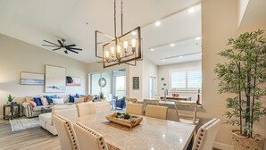 A spacious living room with a large dining table, a sofa set, and a kitchen in the background. - Elegant Naples Condo w/ Golf View & Community Pool (Naples)