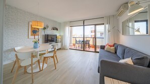 A modern living room with a grey sofa, a dining table with chairs, and a balcony with a view.