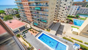 A high-rise building with multiple balconies, a swimming pool, and a view of the sea.