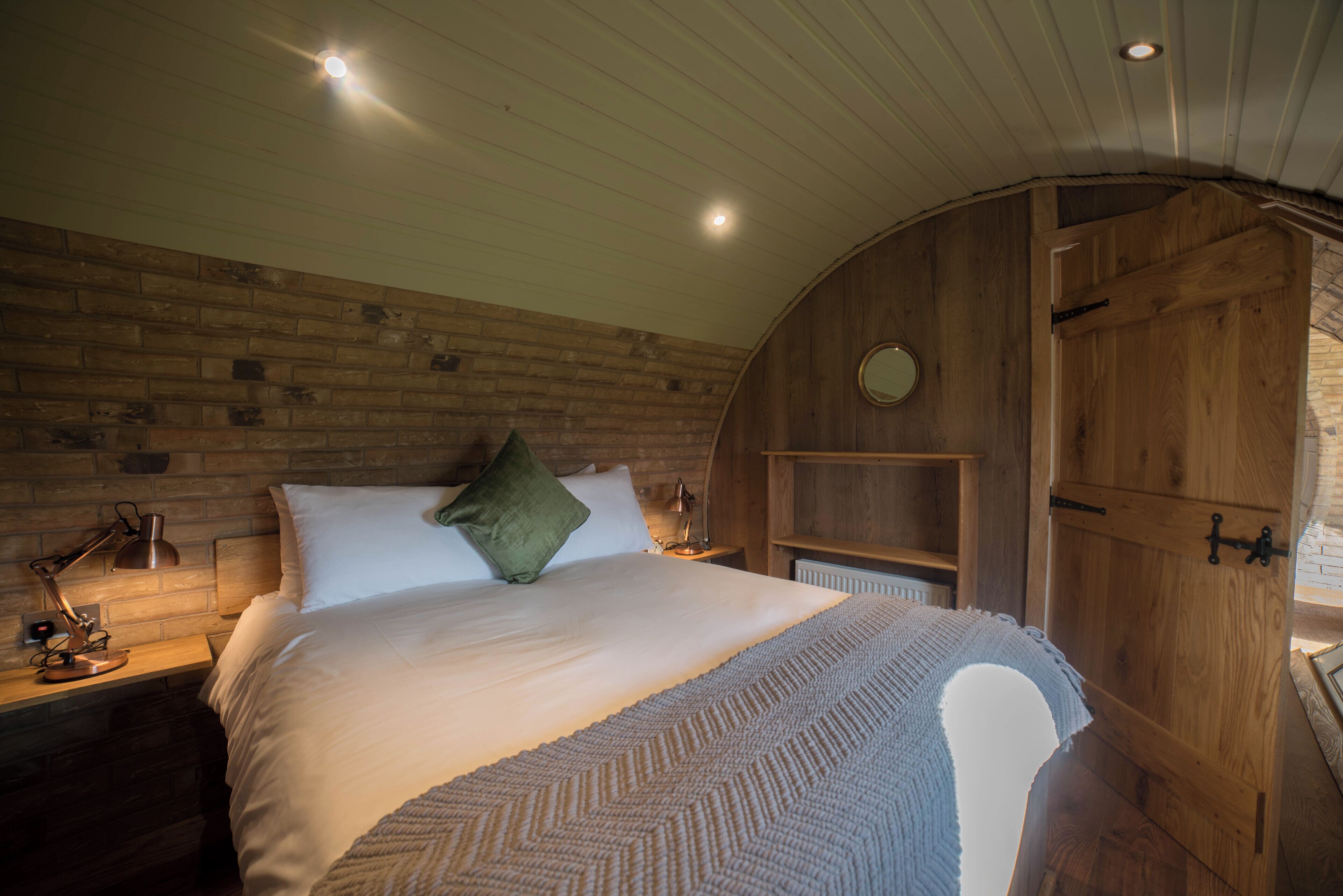 Ein gemütliches Schlafzimmer mit einem Holz-Kopfteil, einem Bett mit weißen Leinen, einem grünen Kissen und einer Nachttischlampe.