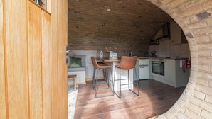 Una cocina con un arco de ladrillo, suelo de madera y dos taburetes de bar.