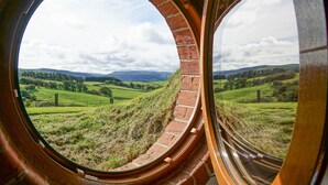 Vista a través de una ventana circular con arcos de ladrillo, que da a un paisaje verde con campos y colinas distantes.