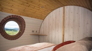 Un dormitorio con ventanal circular, techo de madera y cama con almohadones.