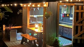 An outdoor dining area with a wooden table and chairs, surrounded by a wooden fence and string lights. - Boutique Luxury Bell Tent Near Torpoint (Torpoint)
